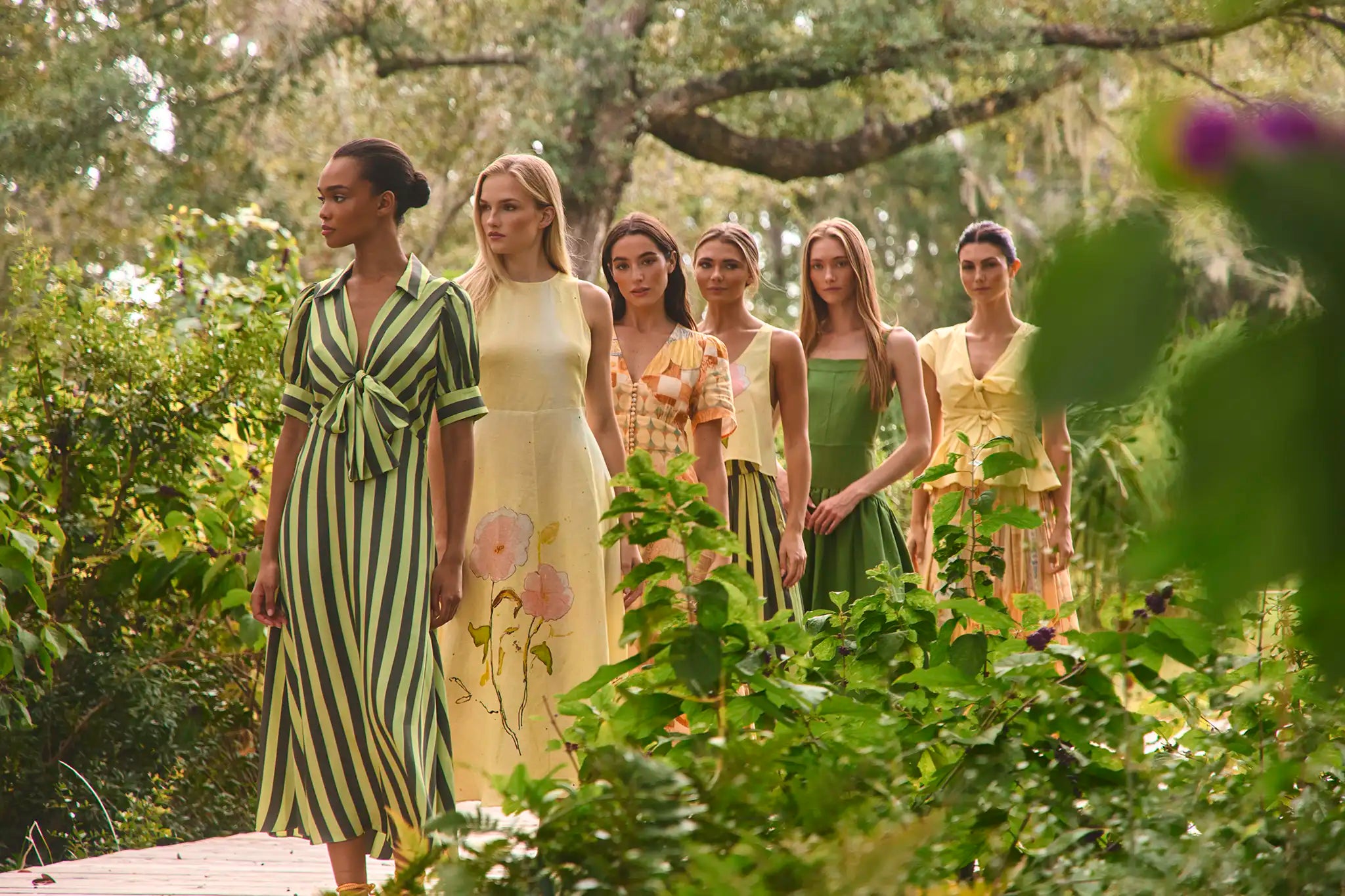 Group of women in stylish dresses standing in a forest setting