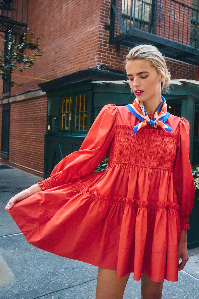 The Arley Dress is a trapeze mini dress with a smocked panel, a ruffle-edge skirt, and long sleeves.