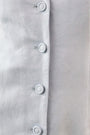 close up of Vest style mini dress in light blue with button front closure and pleated sweep panel.