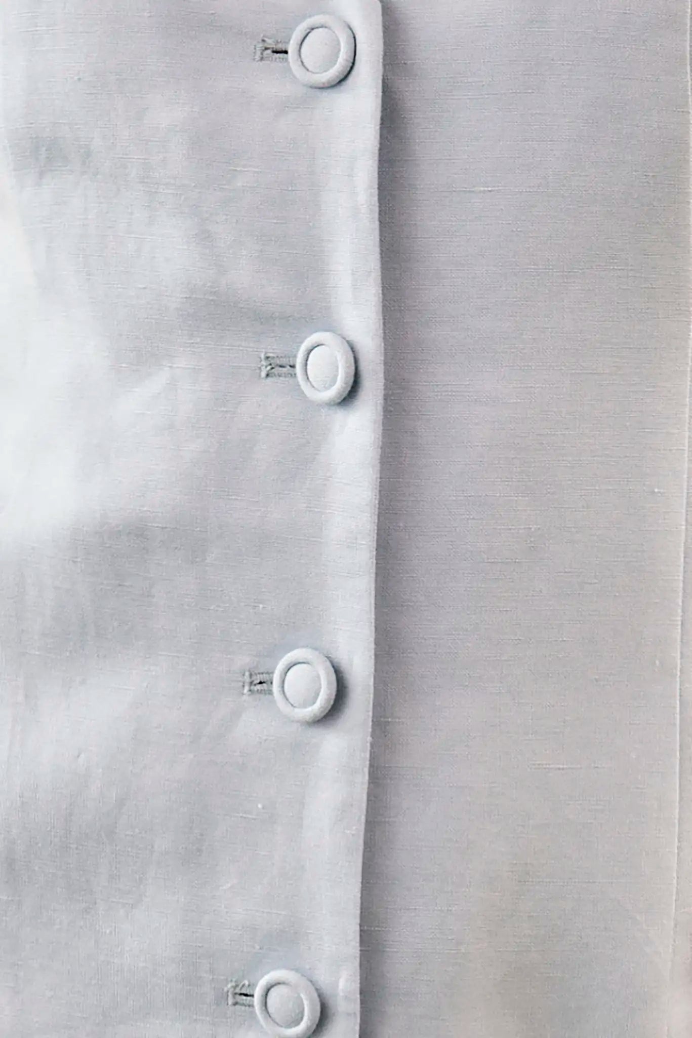 close up of Vest style mini dress in light blue with button front closure and pleated sweep panel.