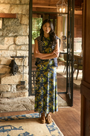 The Barker Dress in Primrose posed in front of fireplace and wood cabin.