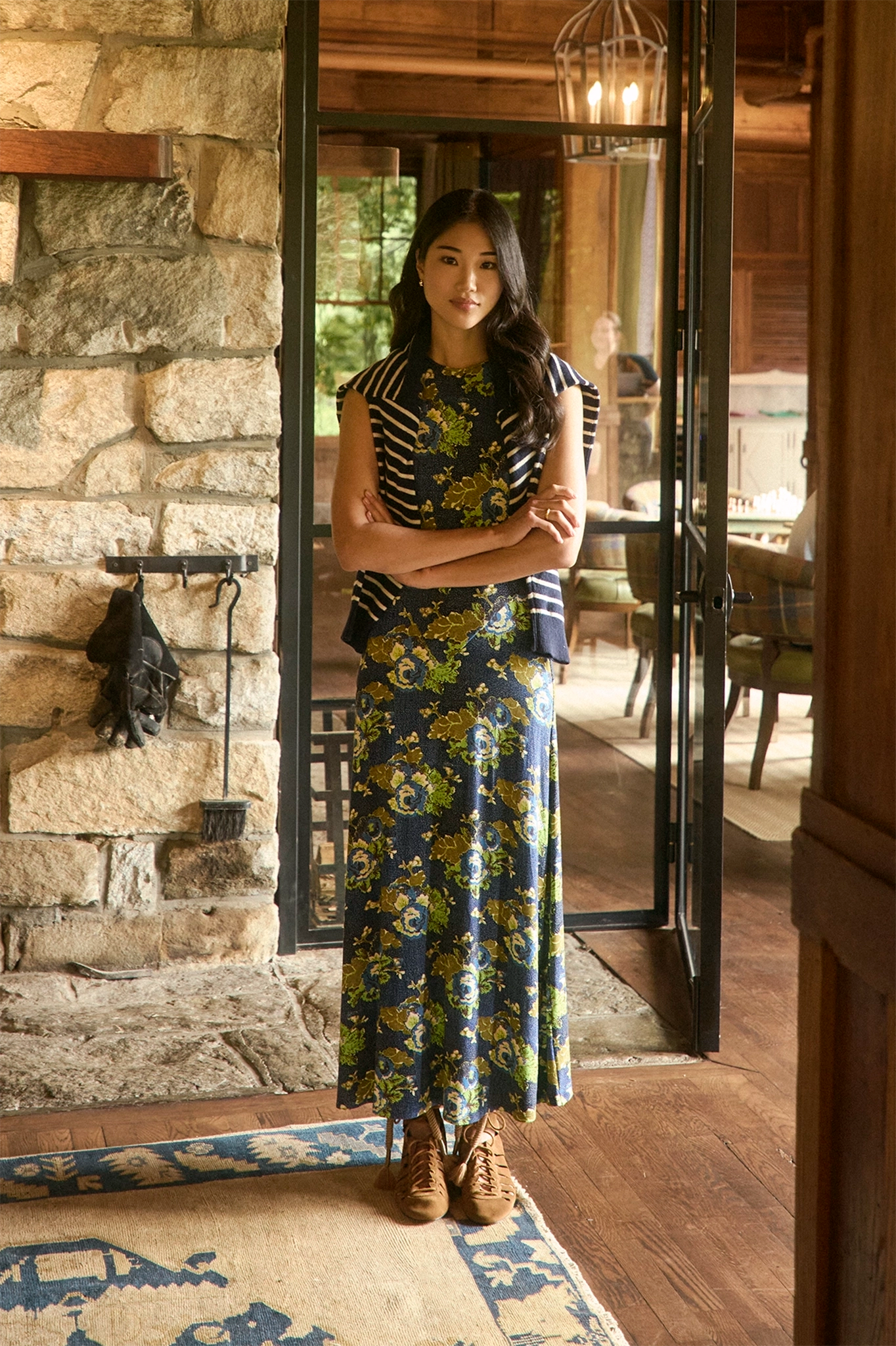 The Barker Dress in Primrose posed in front of fireplace and wood cabin.