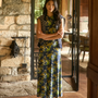 The Barker Dress in Primrose posed in front of fireplace and wood cabin.