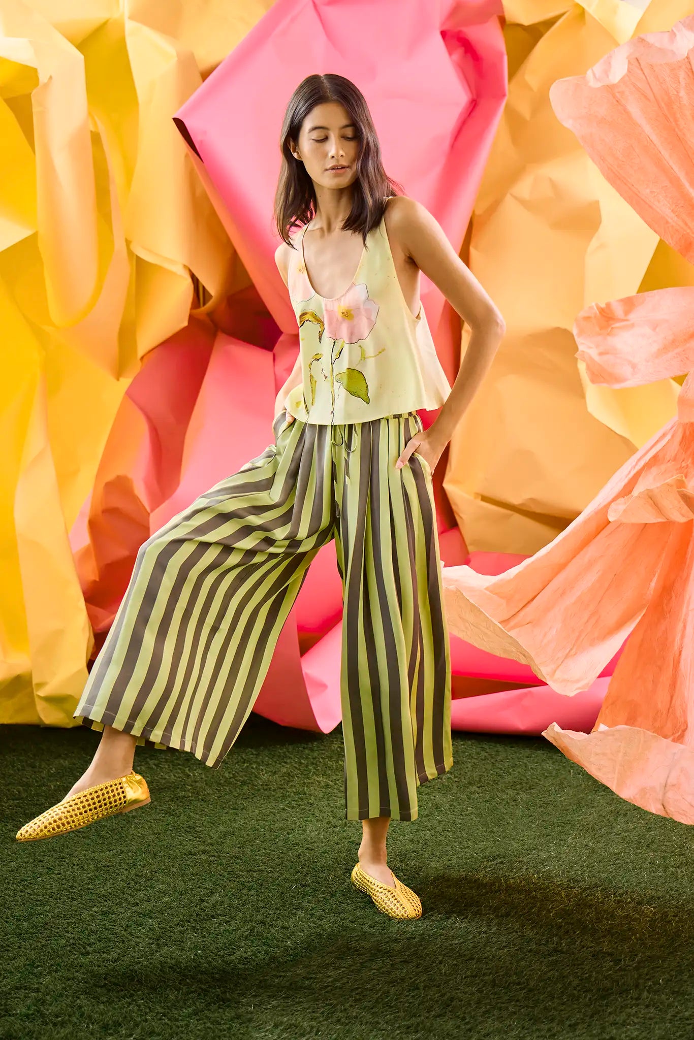 The Carsyn Tank in Quiet Bloom paired with Cyprus Pant in Evergreen Stripe in front of colorful wall.