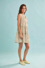 The Fawn Dress in Coral Multi paired with pale yellow shoes on a blue background.