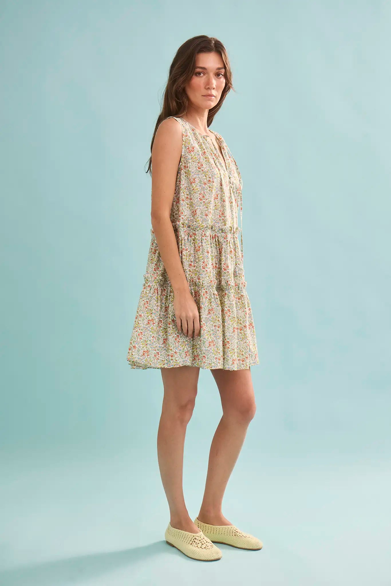 The Fawn Dress in Coral Multi paired with pale yellow shoes on a blue background.