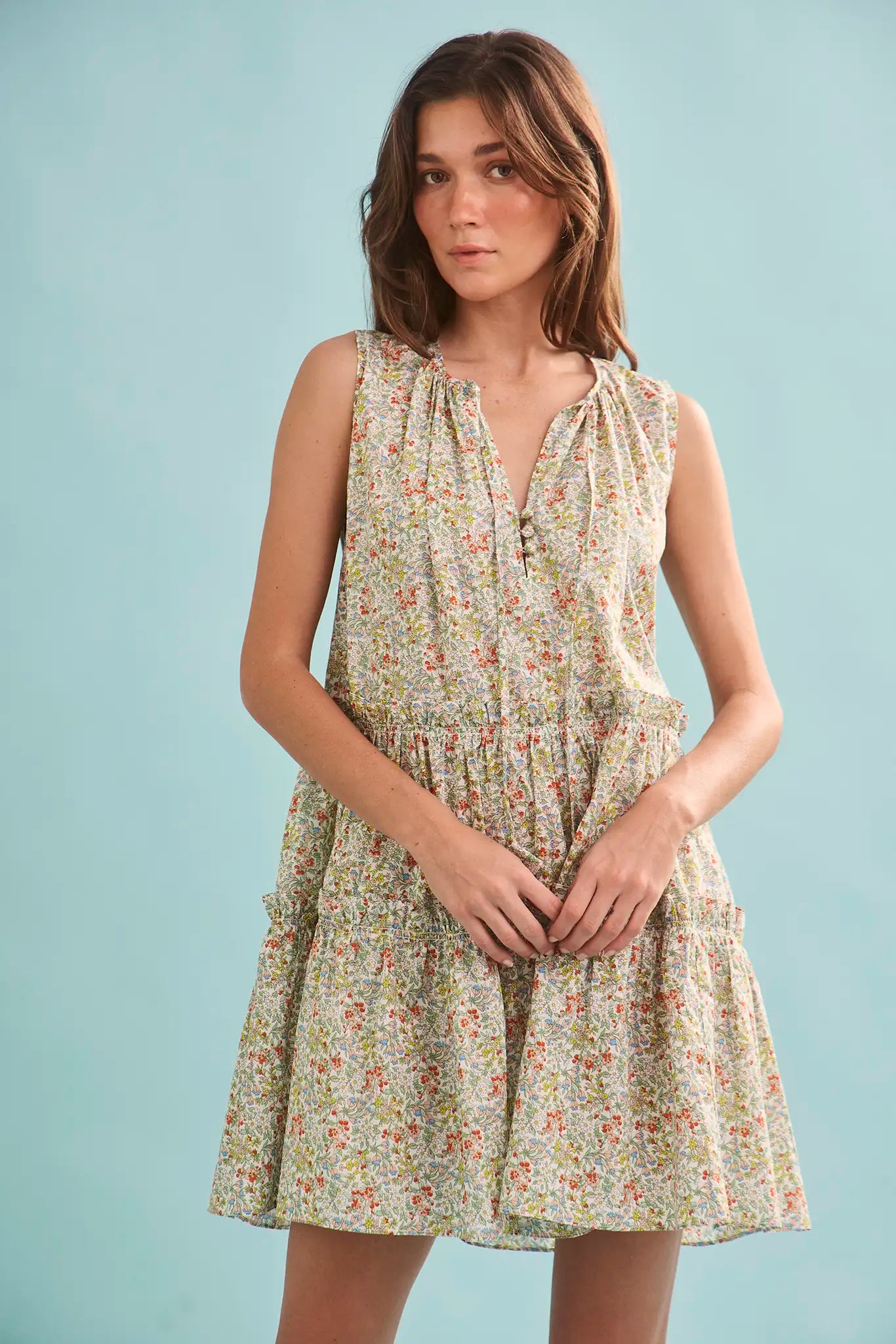The Fawn Dress in Coral Multi paired with pale yellow shoes on a blue background.