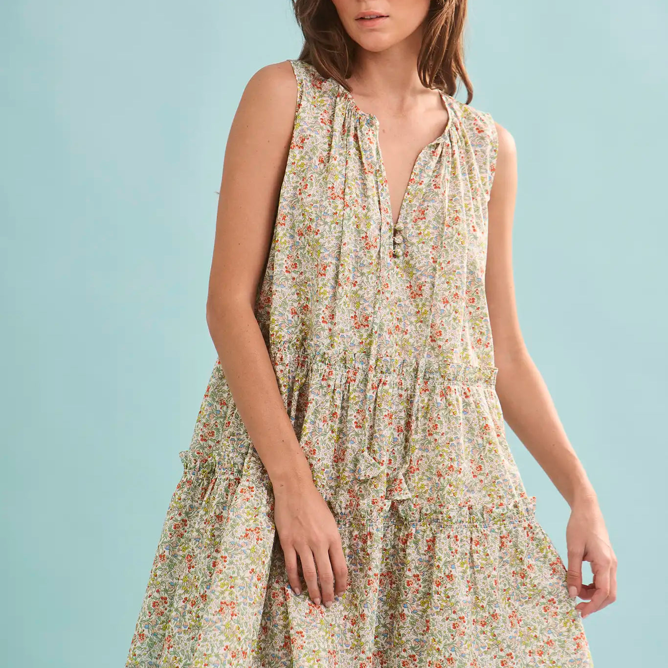 The Fawn Dress in Coral Multi paired with pale yellow shoes on a blue background.