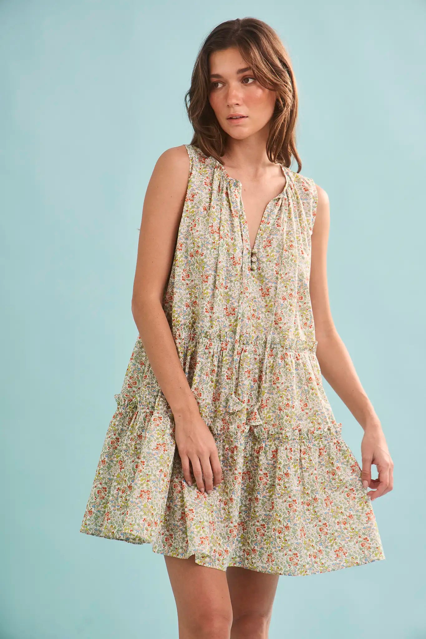 The Fawn Dress in Coral Multi paired with pale yellow shoes on a blue background.