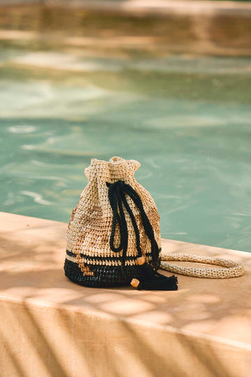 The hand crochet Raffia Bucket Bag has a palm tree design with a convenient drawstring closure.
