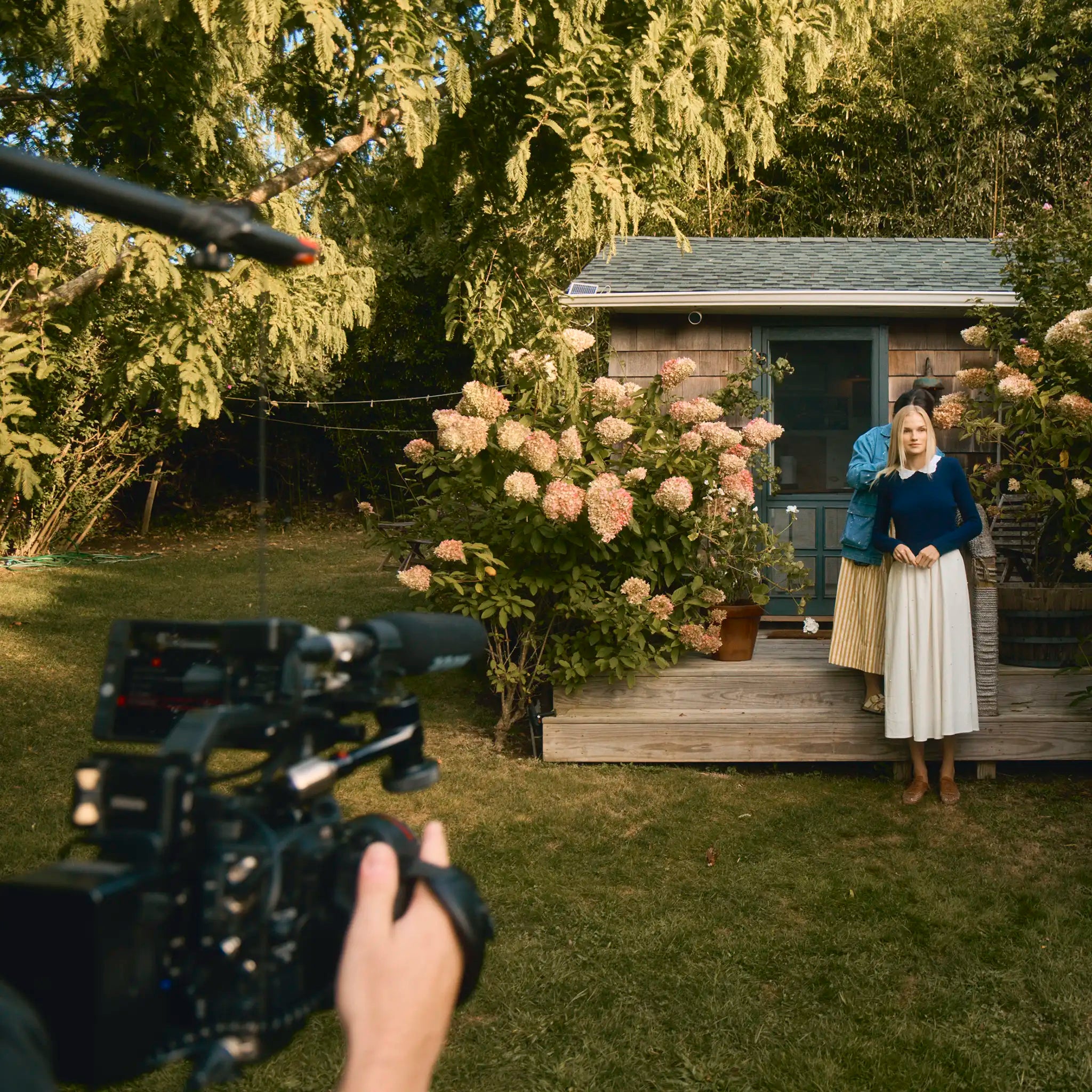 Person filming another person in a garden setting with a camera.