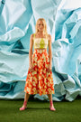 A full-length pleated orange and yellow printed skirt with a fixed waistband and functional pockets.