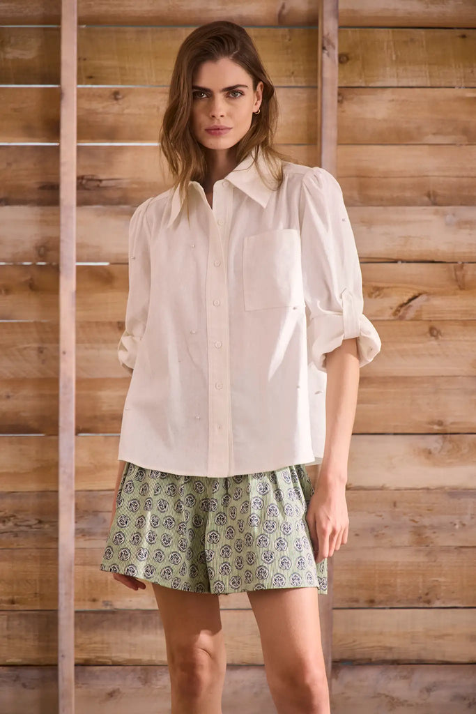 White linen long-sleeve collared shirt with roll-tab sleeves and pearl embellishments.