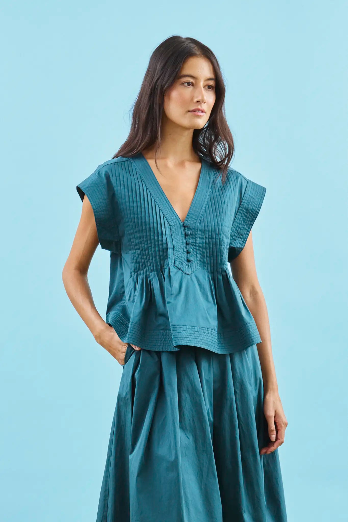 A cropped, boxy top, v-neckline, delicate pintuck detailing and short banded sleeve in petrol green.