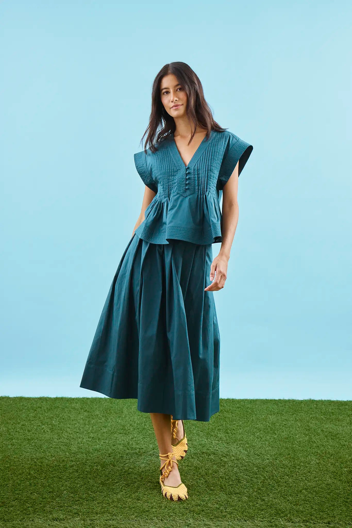 A cropped, boxy top, v-neckline, delicate pintuck detailing and short banded sleeve in petrol green.