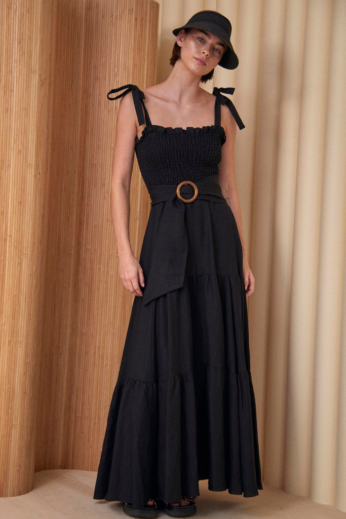 The Lydia smocked maxi dress has tie shoulder straps, a wood buckle sash, and tiered hems.