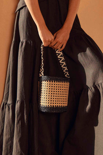 A natural and black cane bucket bag, with crochet accents and a black and white woven strap.