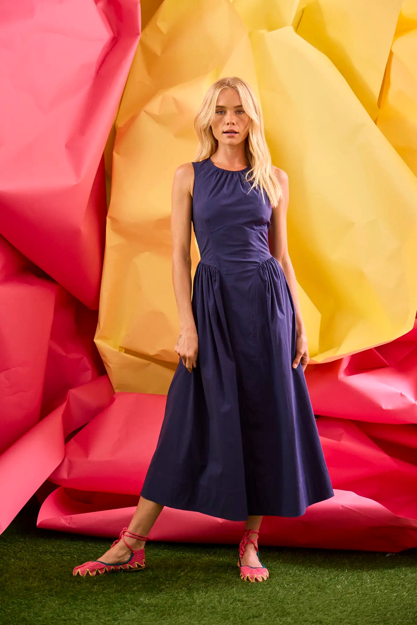 A sleeveless midi navy dress with a fitted bustier bodice, crew neckline, and a bustled full skirt.
