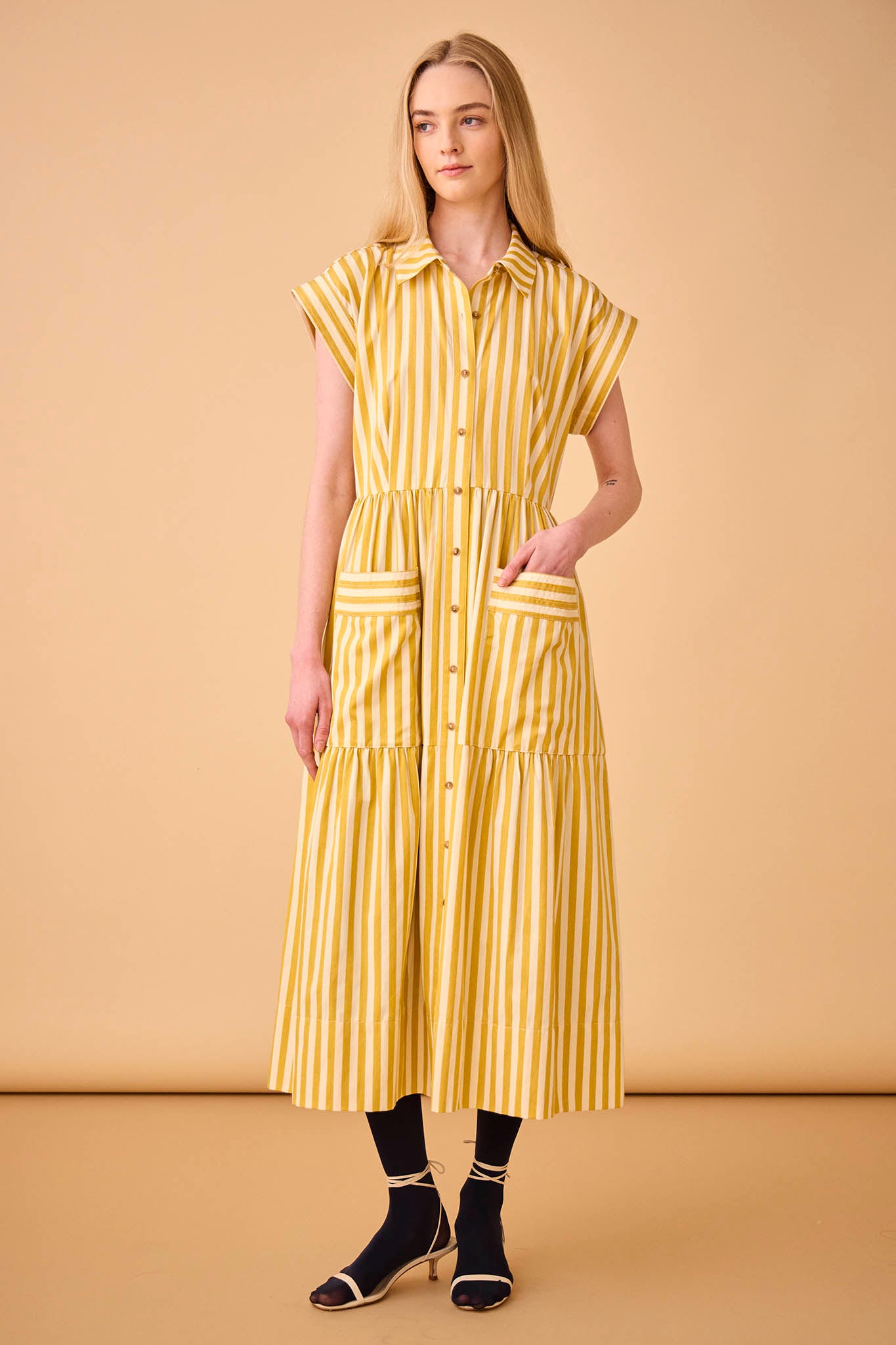 This Sarah dress is a shirt dress with banded cap sleeves, a tiered skirt, and patch front pockets.