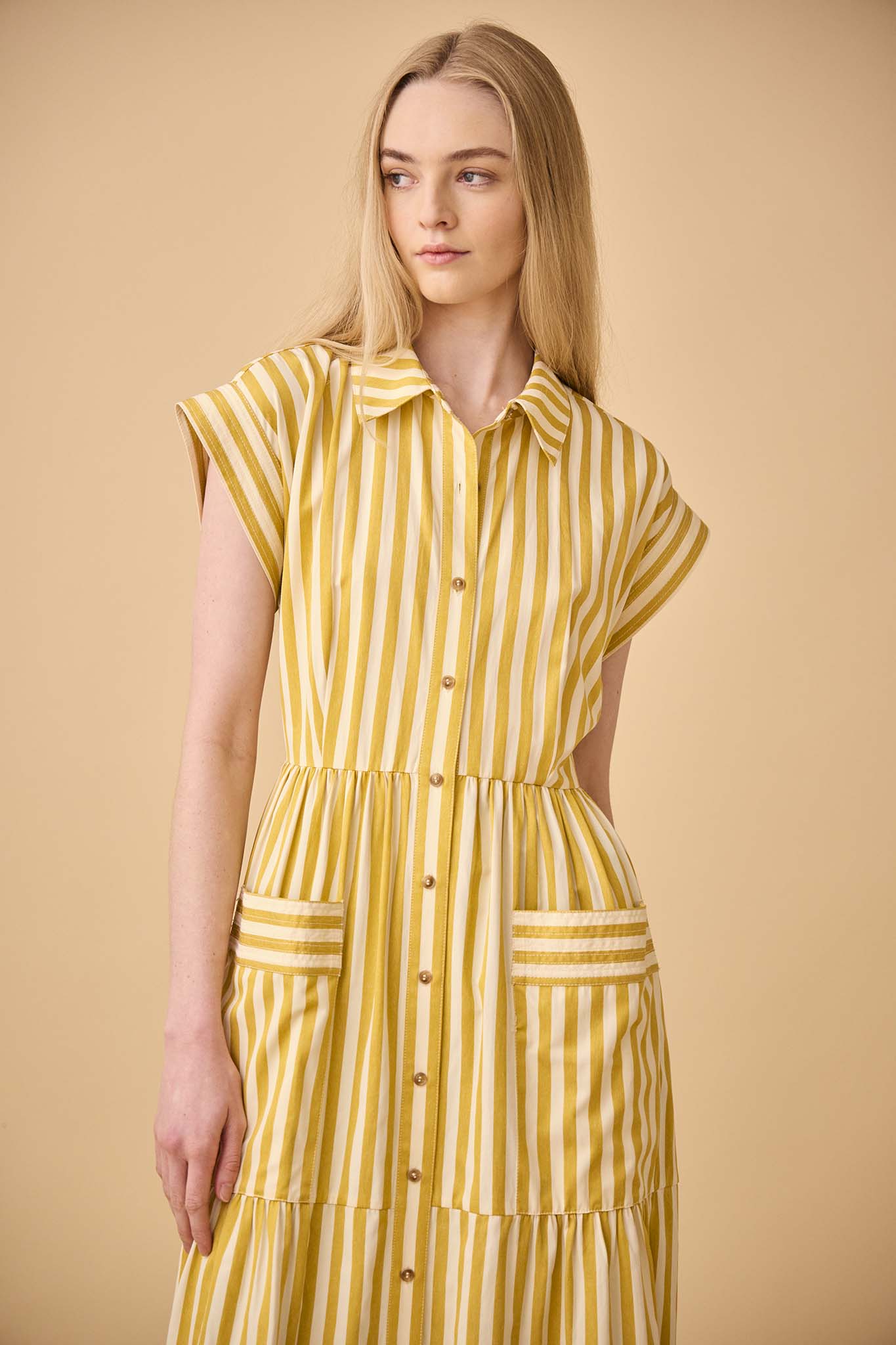 This Sarah dress is a shirt dress with banded cap sleeves, a tiered skirt, and patch front pockets.