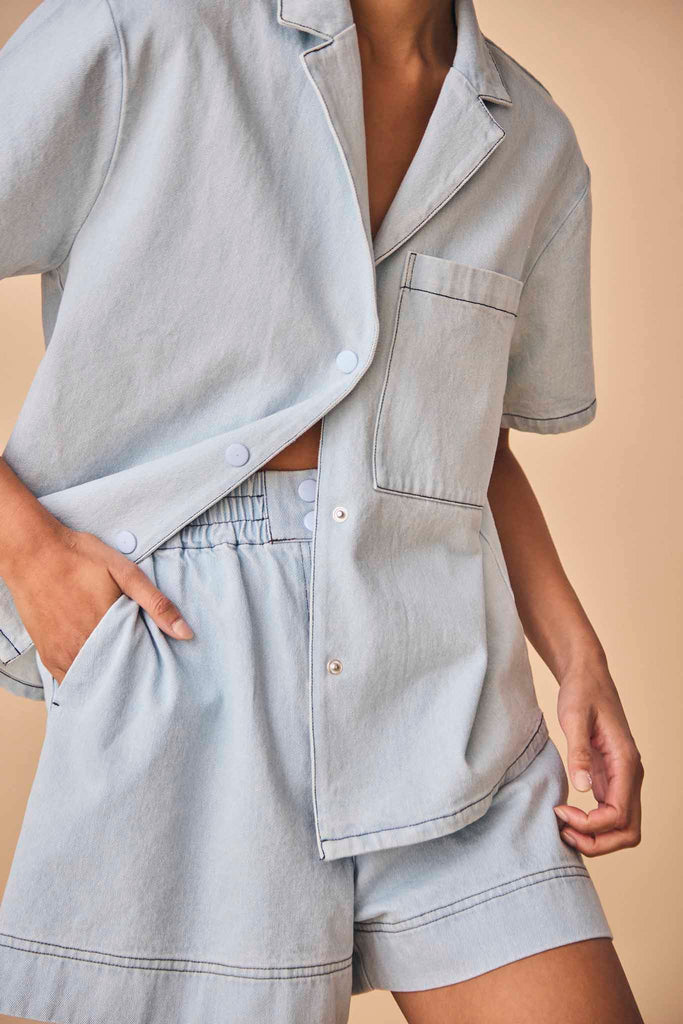 A cotton denim shirt with contrast trim, a patch front pocket, a camp collar and snap buttons.