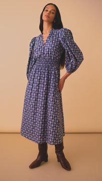 The Violet Dress has a round neckline with buttons, a tie front keyhole, and a smocked waist.