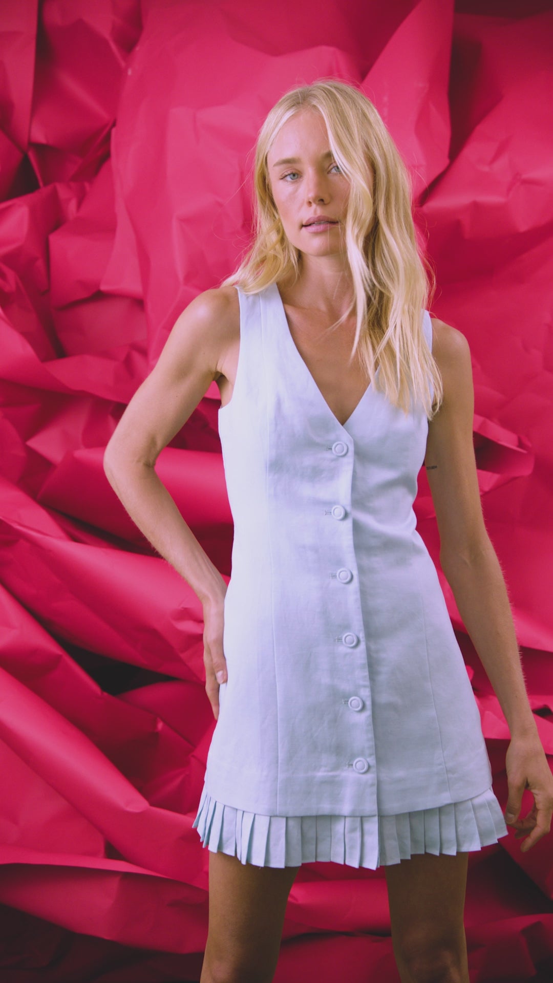 Vest style mini dress in light blue with button front closure and pleated sweep panel.