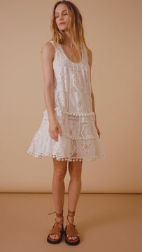 The Maude dress is a mini dress with lace macrame, eyelet embroidery, a drop waist and pom-pom trim.