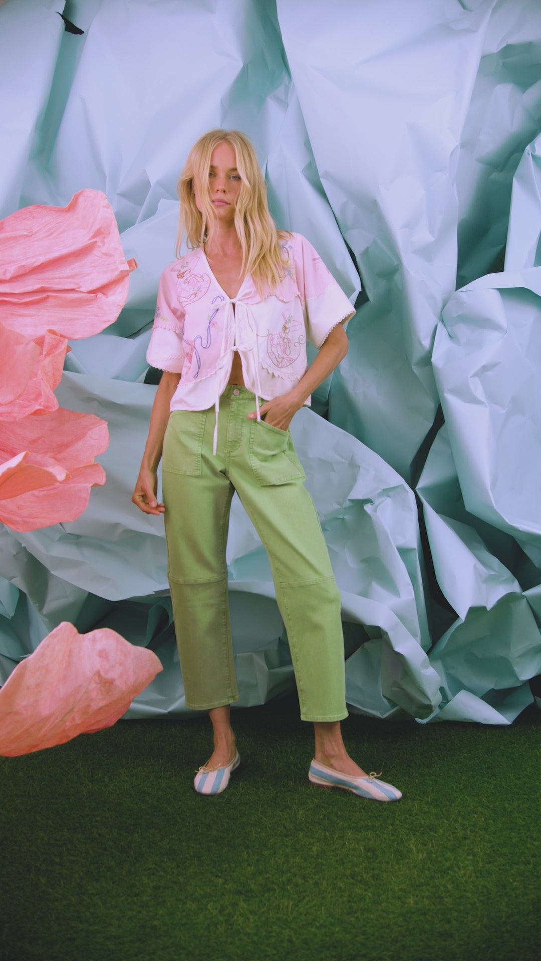 The Bryce Top in Lazy Daisy paired with green Mallory Jeans in front of blue wall.