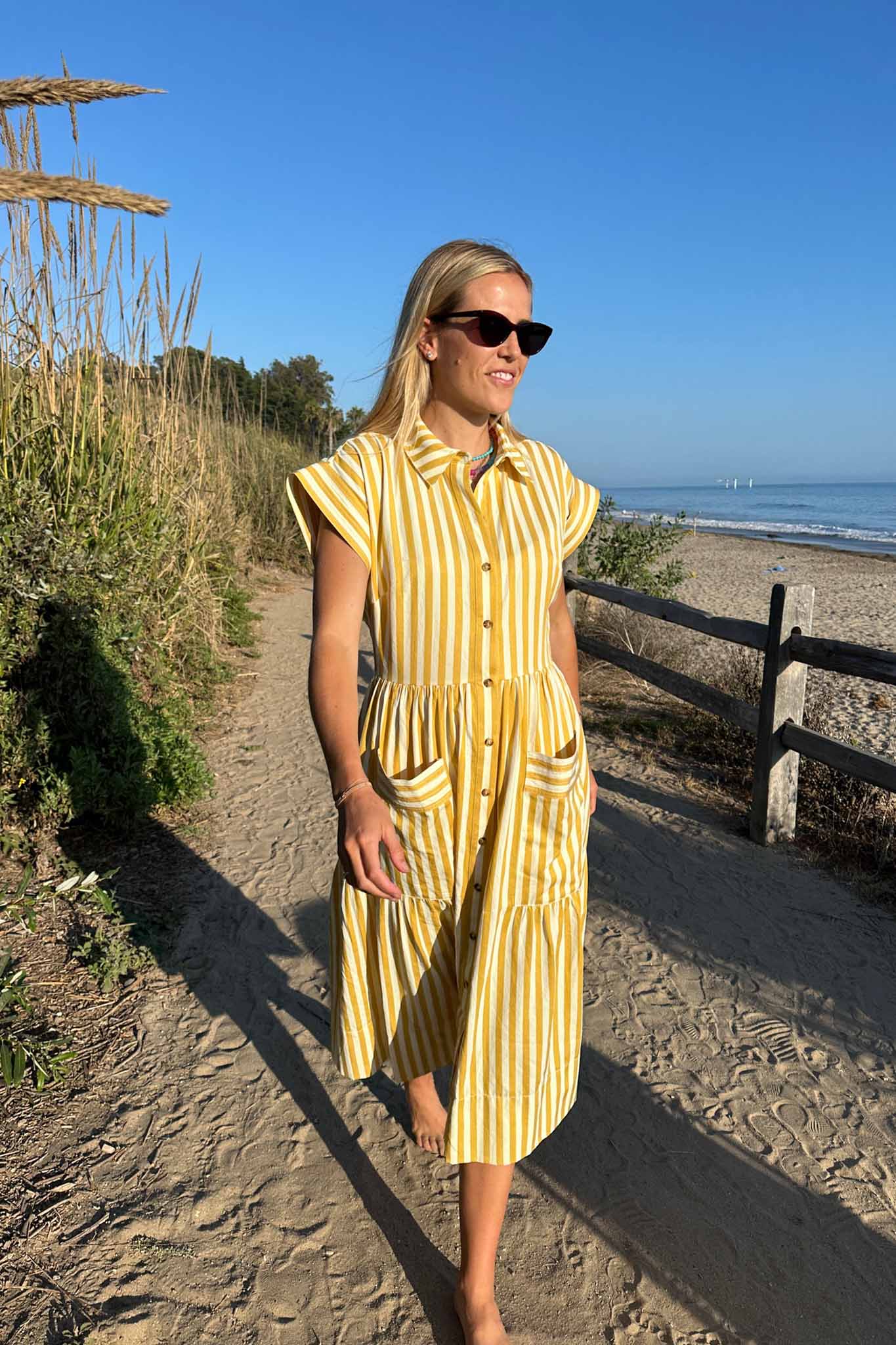 This Sarah dress is a shirt dress with banded cap sleeves, a tiered skirt, and patch front pockets.